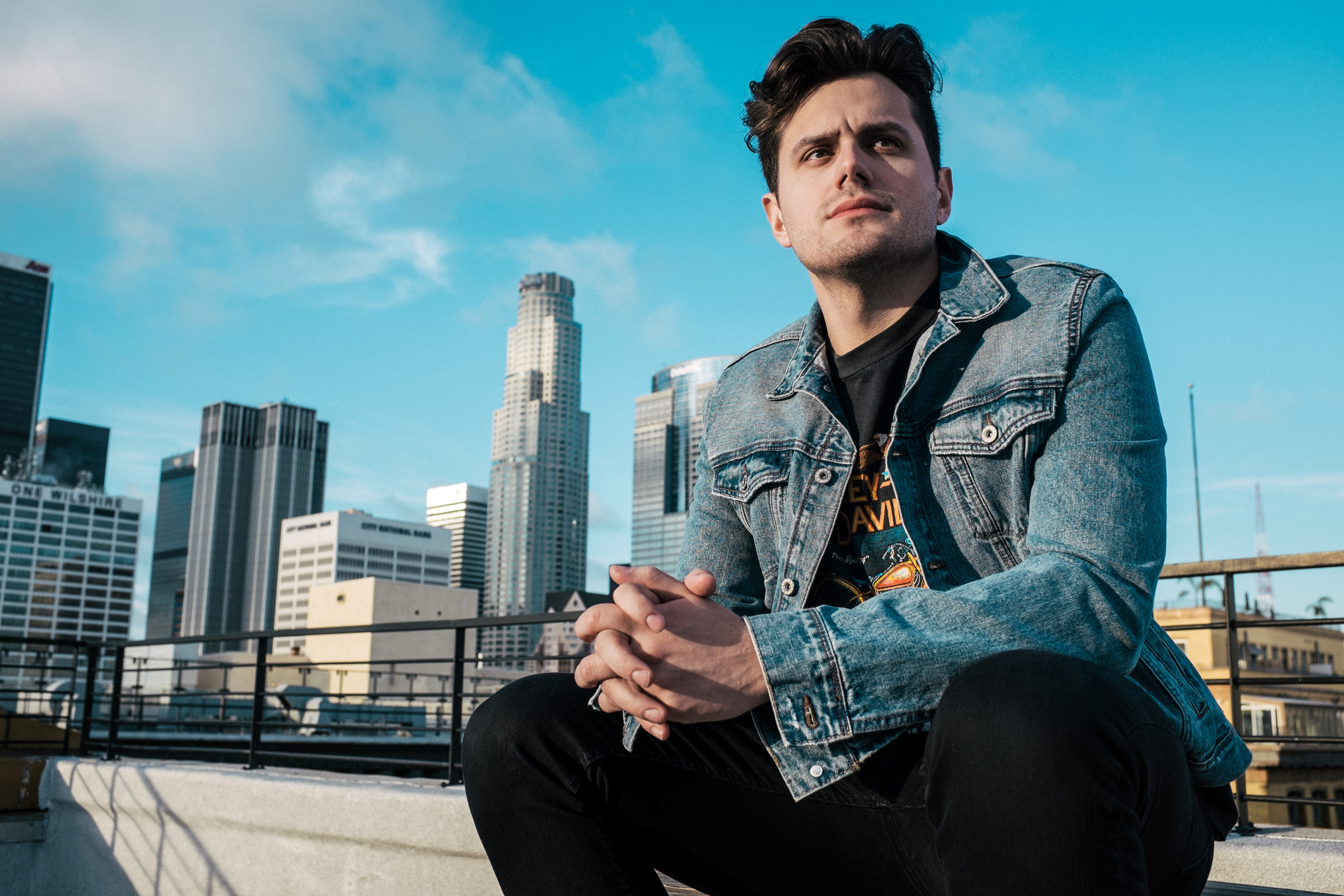Elvis Suarez seated on a rooftop, with the city skyline behind him.